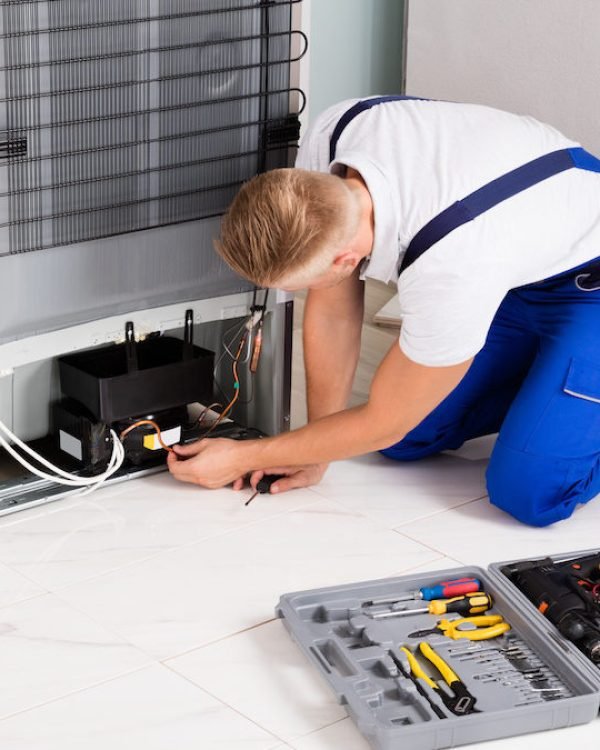 Young Male Technician Checking Refrigerator With Screwdriver